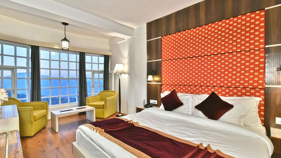 A bedroom with a seating area by the window, offering a mountain view at DLS Hillcrest Resort, Shimla.